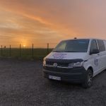 CampEasy campervan parked at a gravel site at sunset, with the sun setting on the horizon casting a warm orange glow across the sky, providing a picturesque end to a day in Iceland.