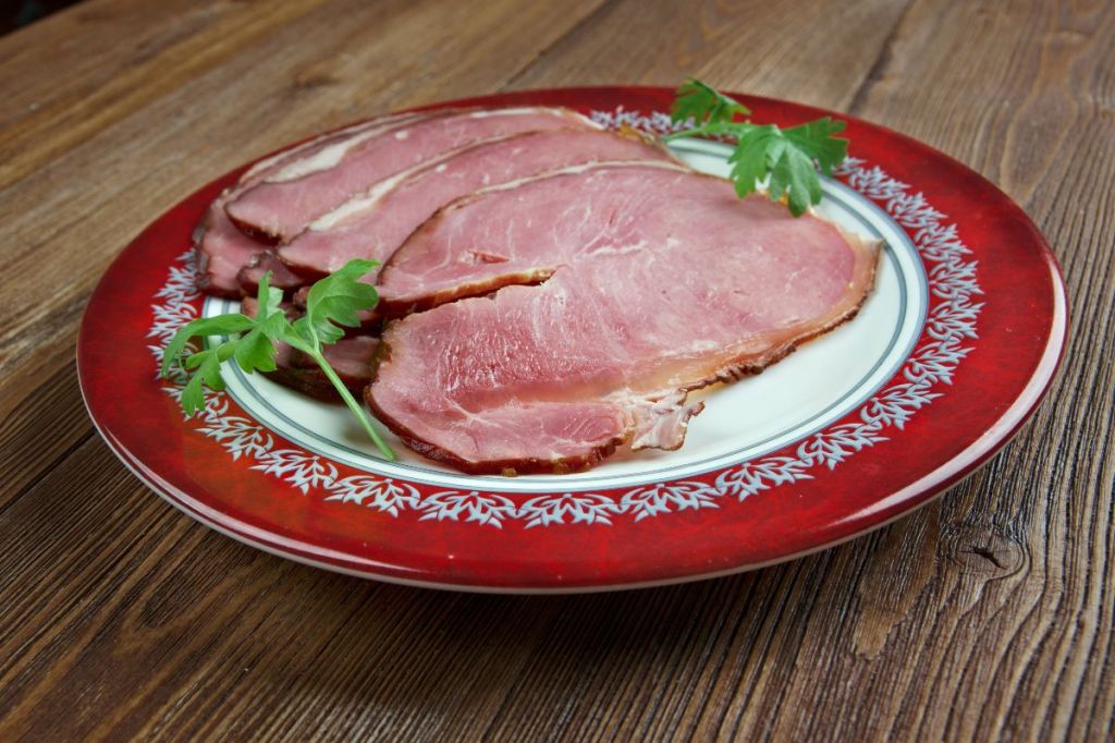 Slices of traditional Icelandic smoked lamb (Hangikjöt) served on a festive red plate, garnished with parsley.