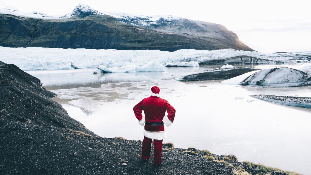 Santa Claus standing on a black volcanic slope overlooking a glacier in Iceland, surrounded by snowy mountains and reflecting icy waters, capturing the unique blend of Christmas spirit and Icelandic nature.