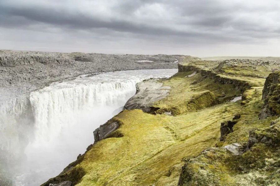 The powerful Dettifoss waterfall in Iceland, cascading over a rocky landscape with a misty, cloudy sky in the background.