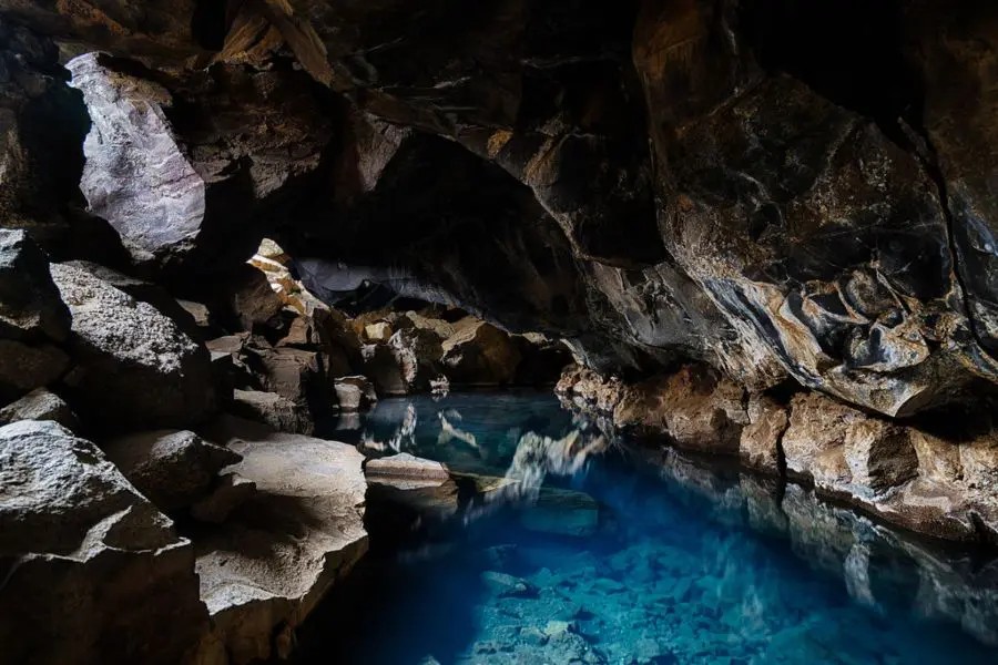 A stunning geothermal cave with clear blue water, surrounded by rugged rock formations, located in northern Iceland.