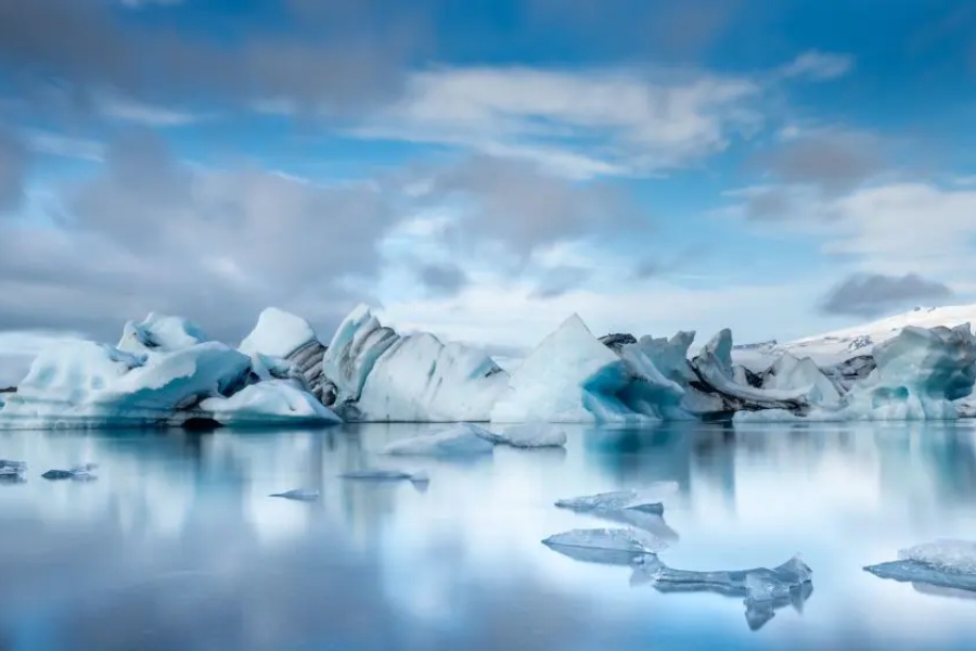 A breathtaking view of Jökulsárlón glacier lagoon in Iceland, with floating icebergs reflecting on the calm water under a cloudy blue sky.