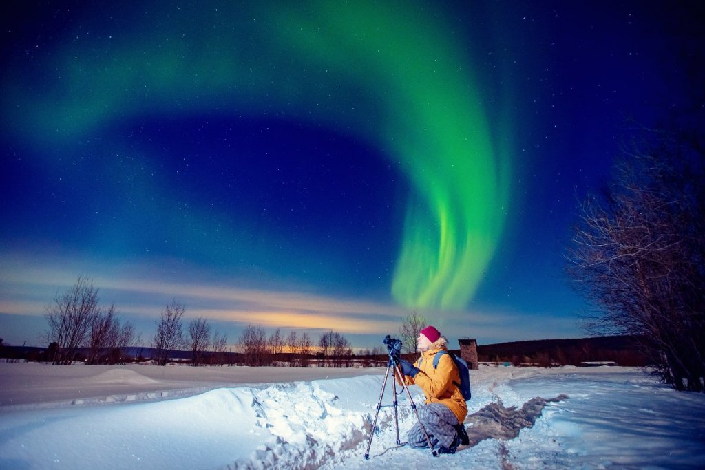 A photographer in winter clothing capturing the Northern Lights with a tripod, under a starry Icelandic sky.