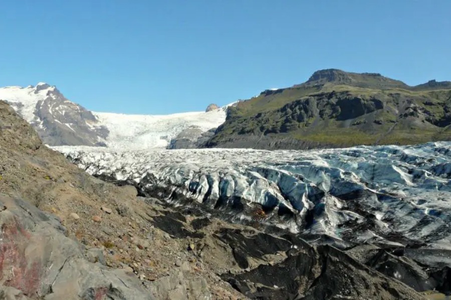 A vast expanse of the Svínafellsjökull glacier in Iceland, surrounded by rugged mountains and clear blue skies.