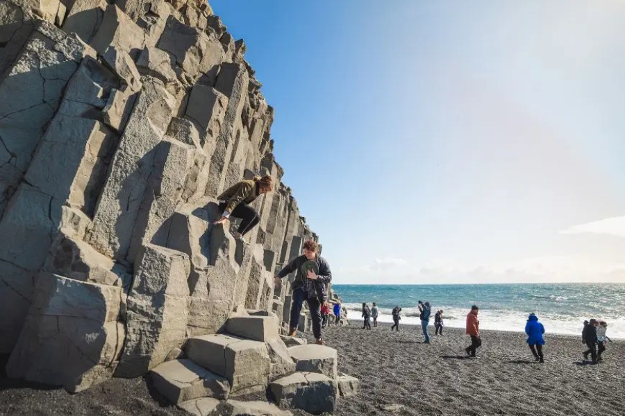 Visitors exploring the black sand beach of Reynisfjara, with basalt rock formations and the ocean stretching into the horizon.