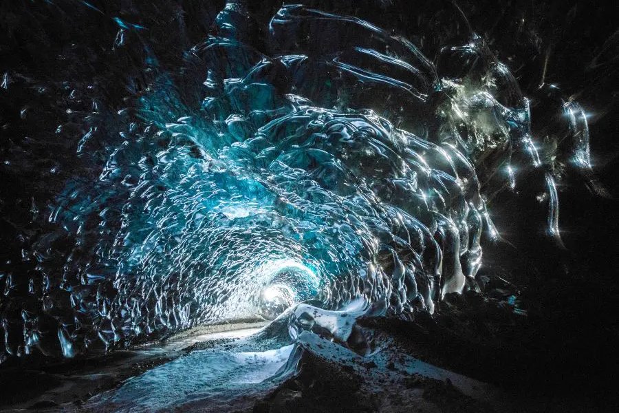 A mesmerizing ice cave in Iceland, featuring glistening blue and white ice formations that create a tunnel-like appearance.