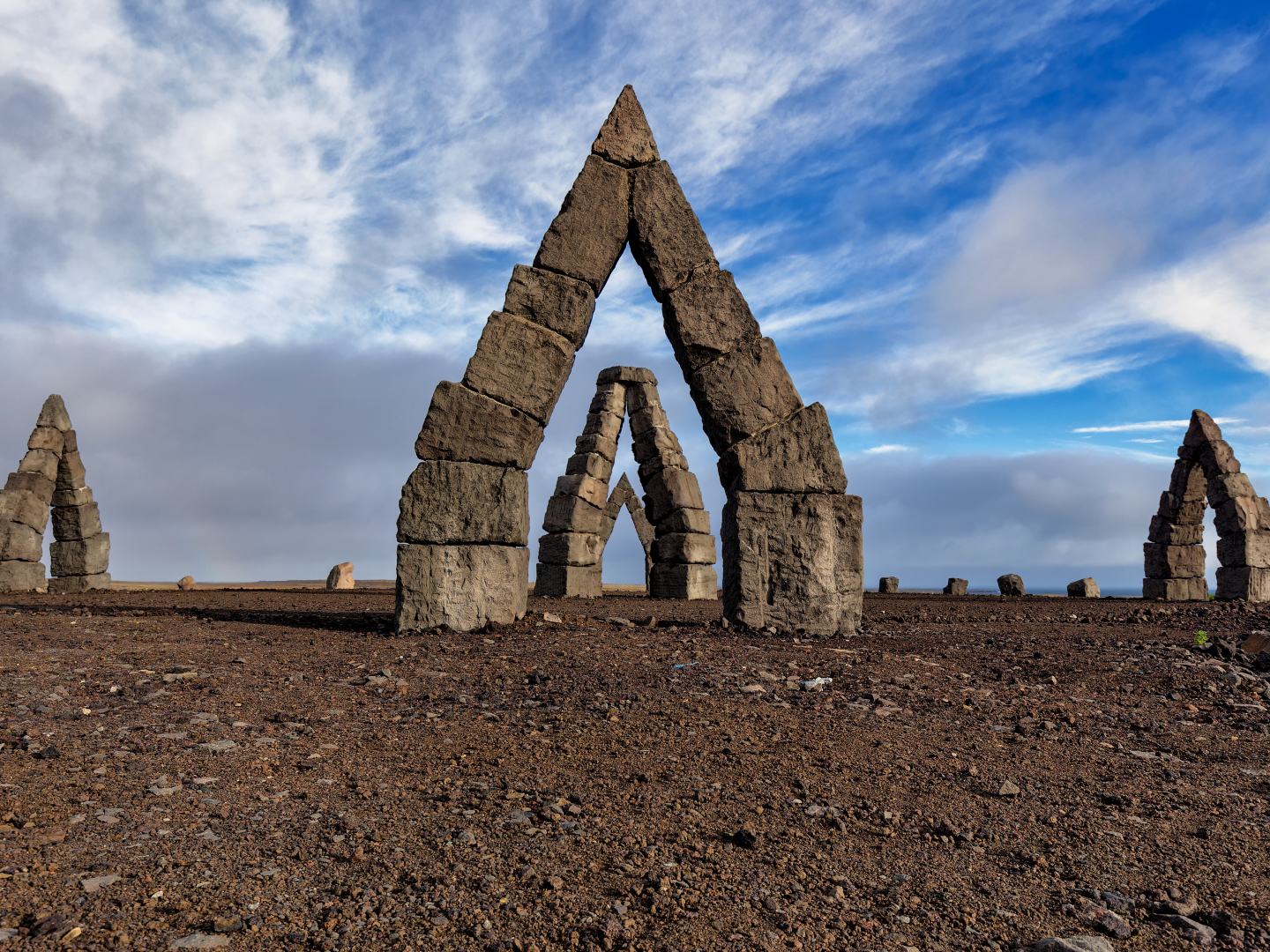 Stone arches form triangular shapes on a barren landscape under a partly cloudy blue sky. The scene conveys a sense of mystery and solitude.