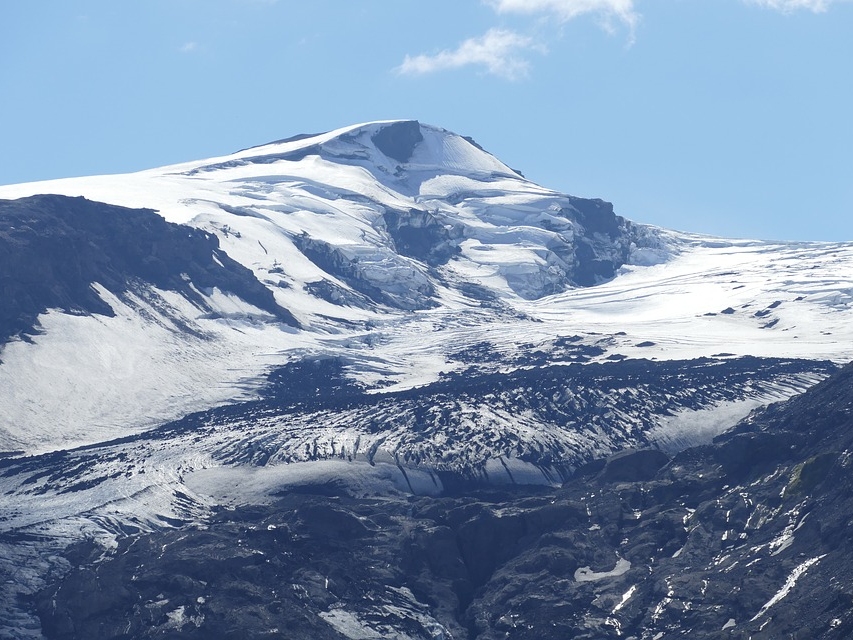 Snow-covered mountain peak under a clear blue sky. The image showcases contrasting white snow against dark rock, conveying a sense of serenity and majesty.