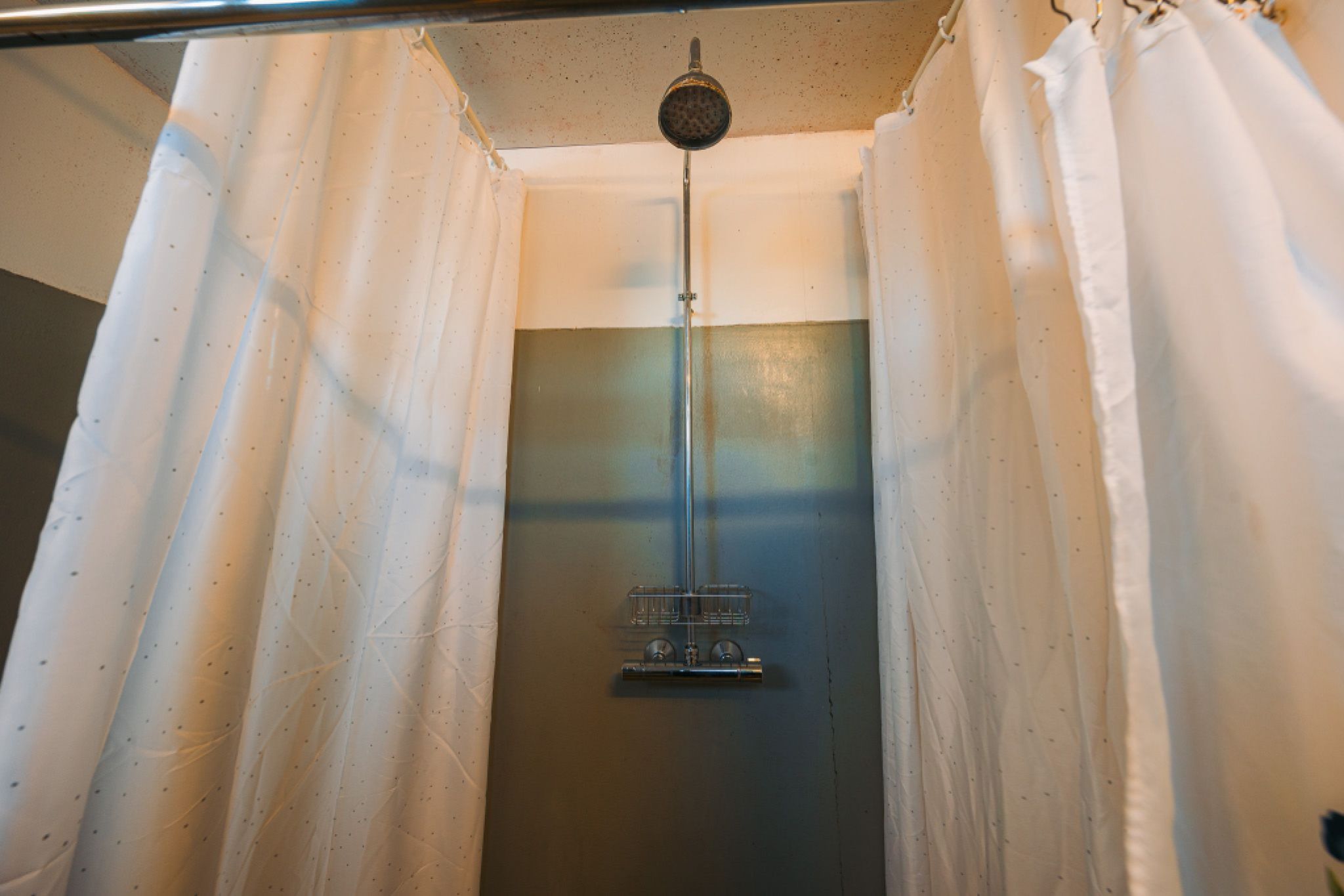 Simple shower setup with a metal showerhead and fixture against a plain wall, flanked by white curtains.