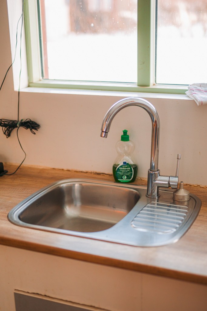 Stainless steel kitchen sink with a tall faucet, liquid soap bottle, and towel nearby.