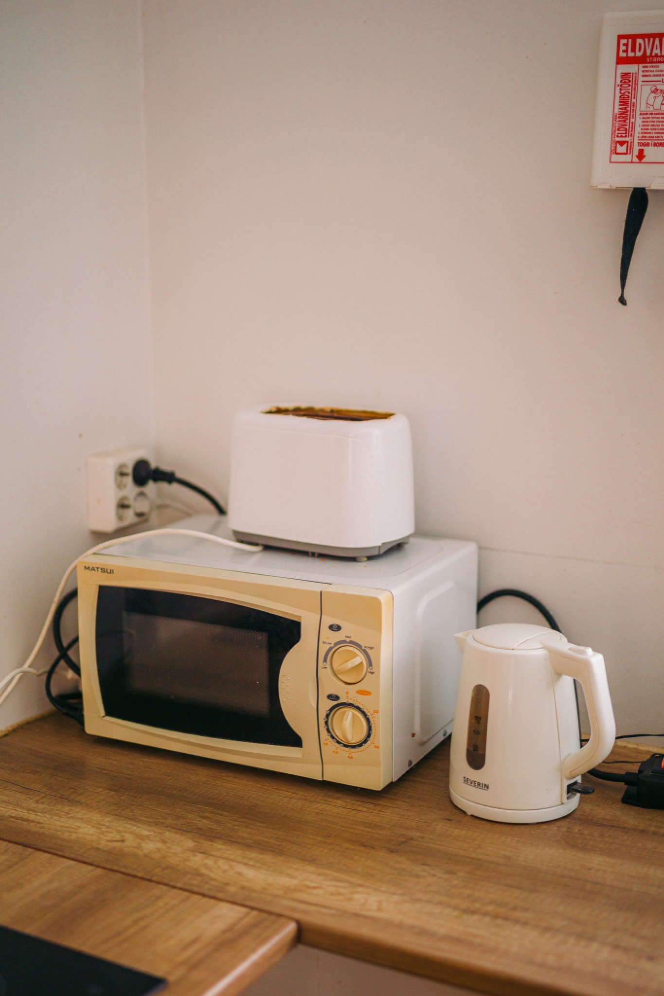 A cozy kitchen corner with a white toaster on a microwave, a kettle nearby on a wooden counter.