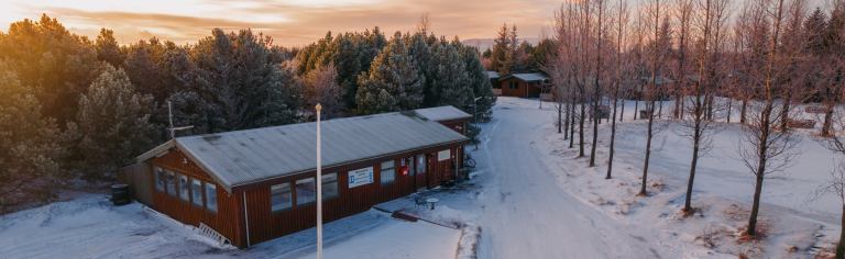 The reception building of the campsite next to dense trees, a snow-covered road, and a field.