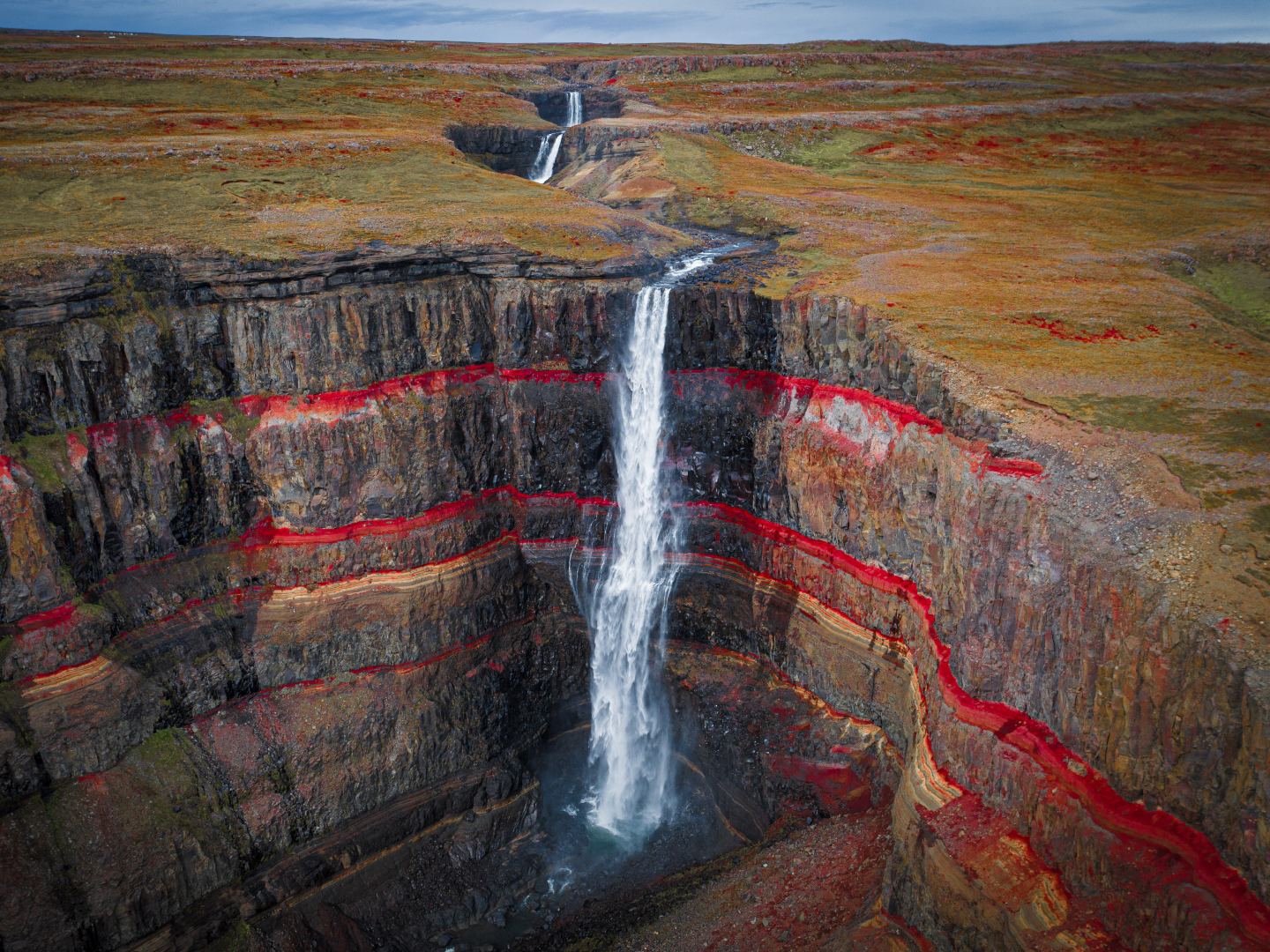 A tall waterfall cascades into a deep canyon with distinct layers of red and brown rock. The dramatic landscape conveys a sense of awe and tranquility.
