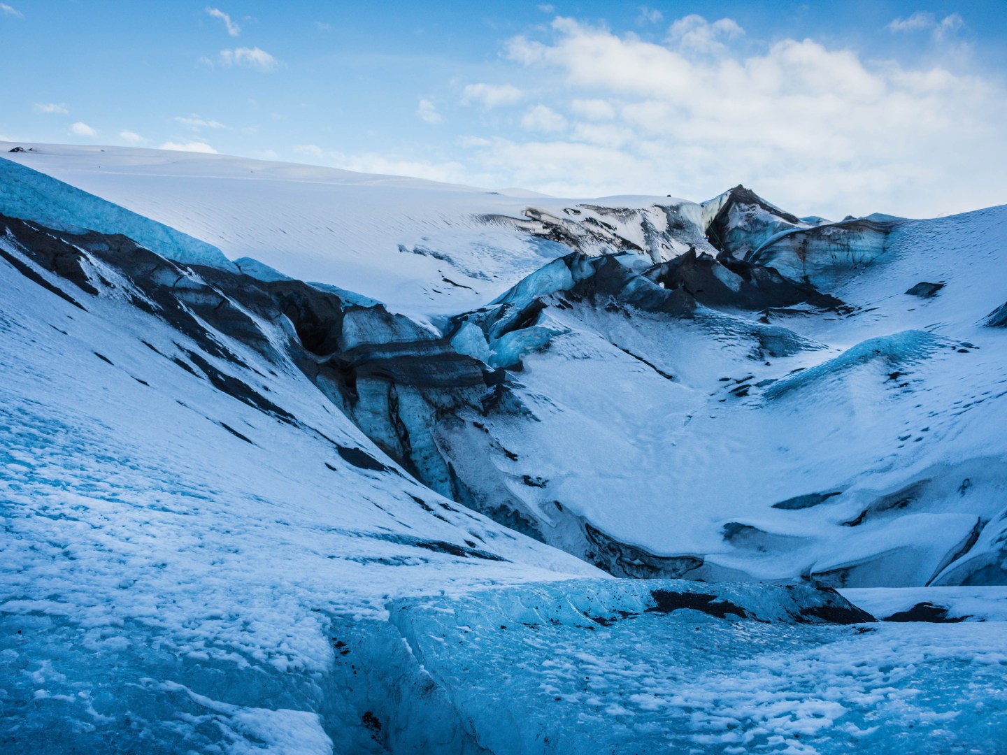 A vast glacier landscape with icy blue and white textures, showing dramatic crevasses under a clear blue sky. The scene conveys a serene and cold atmosphere.