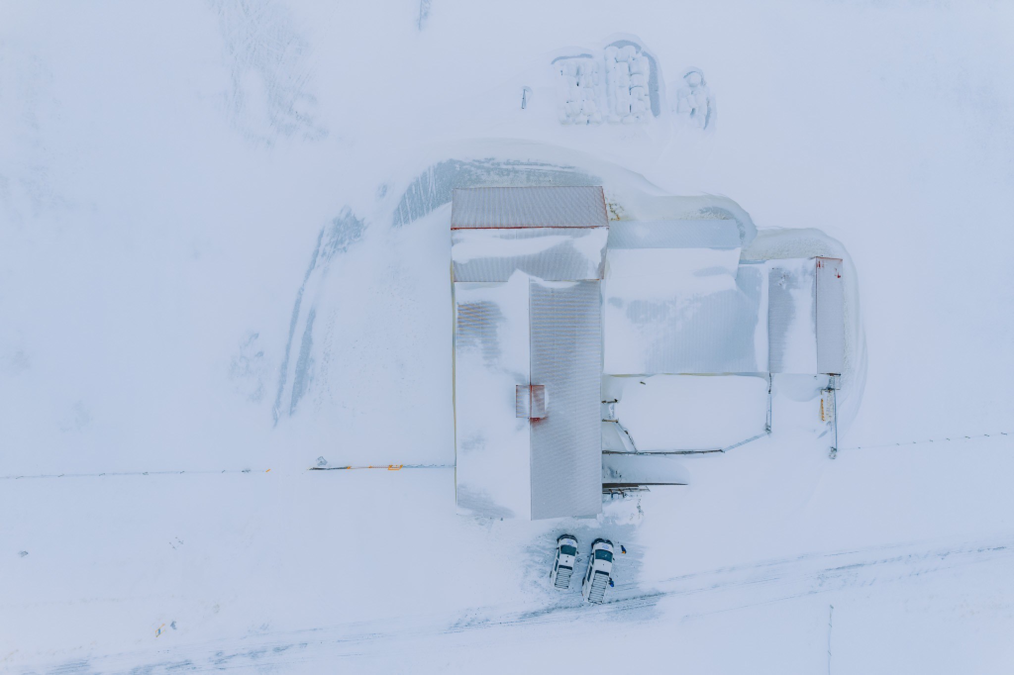Aerial view of a snow-covered building with two parked campers partially buried in snow.