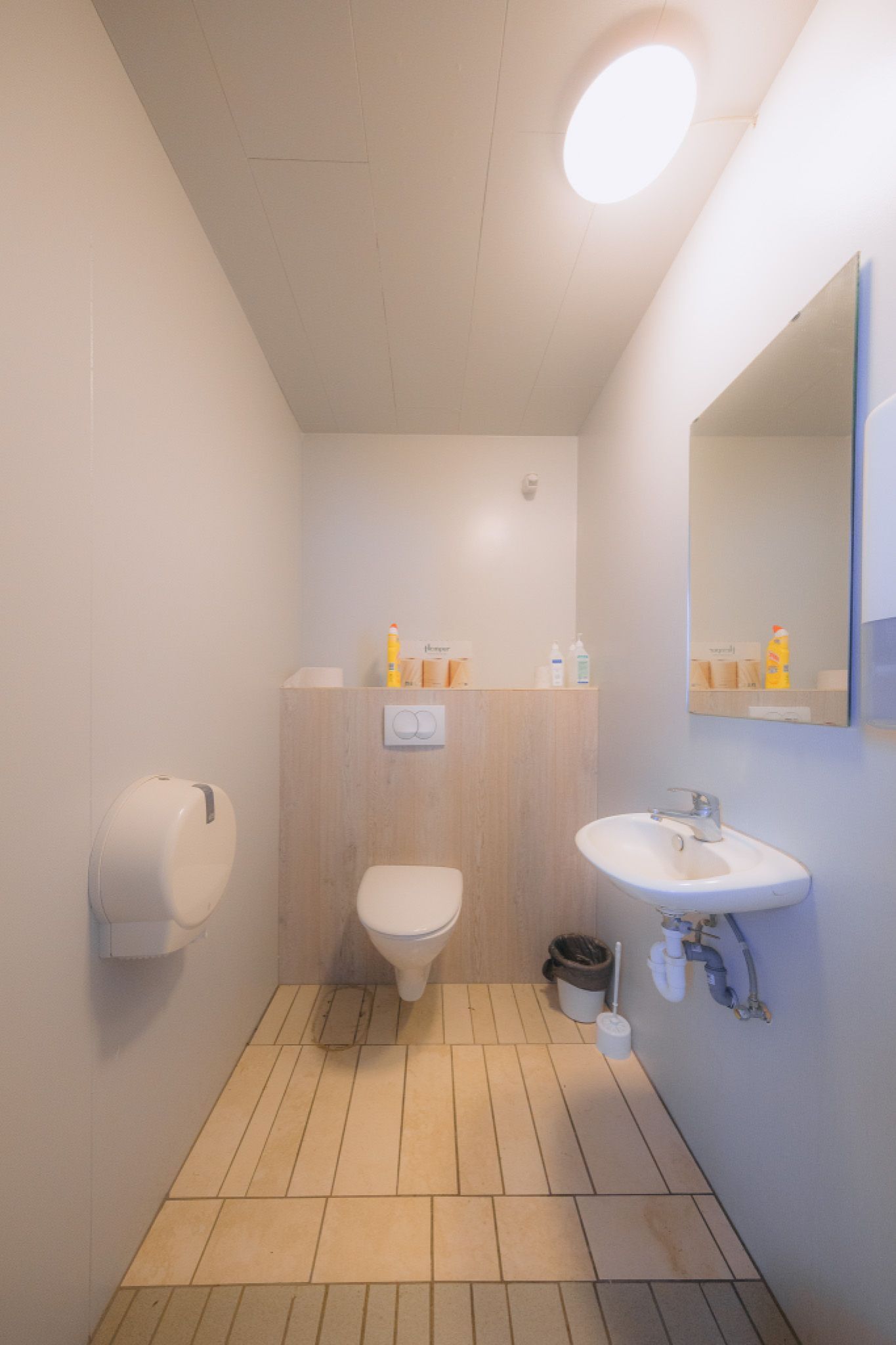 Modern restroom with a wall-mounted toilet and sink. Beige tiles, soft lighting, and a mirror.