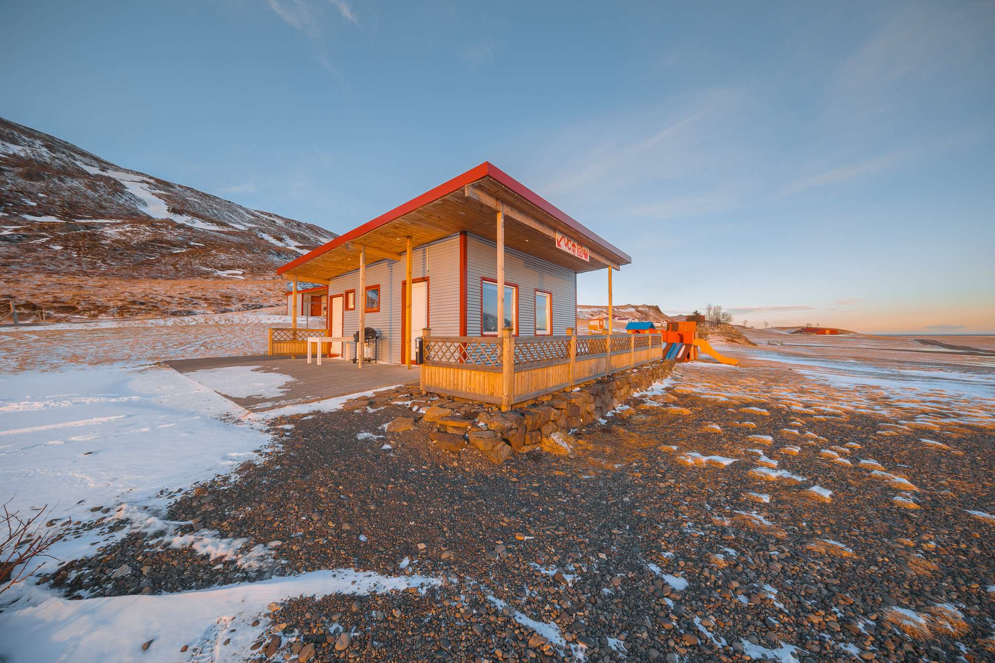 A small, snow-dusted building stands on a rocky landscape under a clear sky.