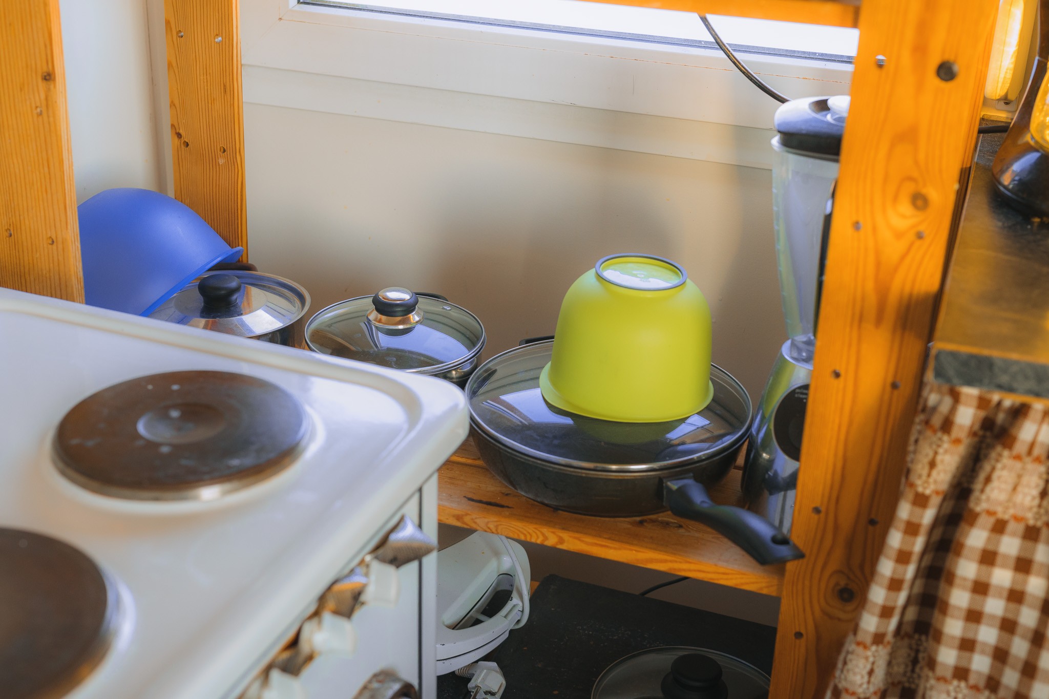 A cluttered kitchen corner with a wooden shelf holding pots, pans, and a bright green bowl.