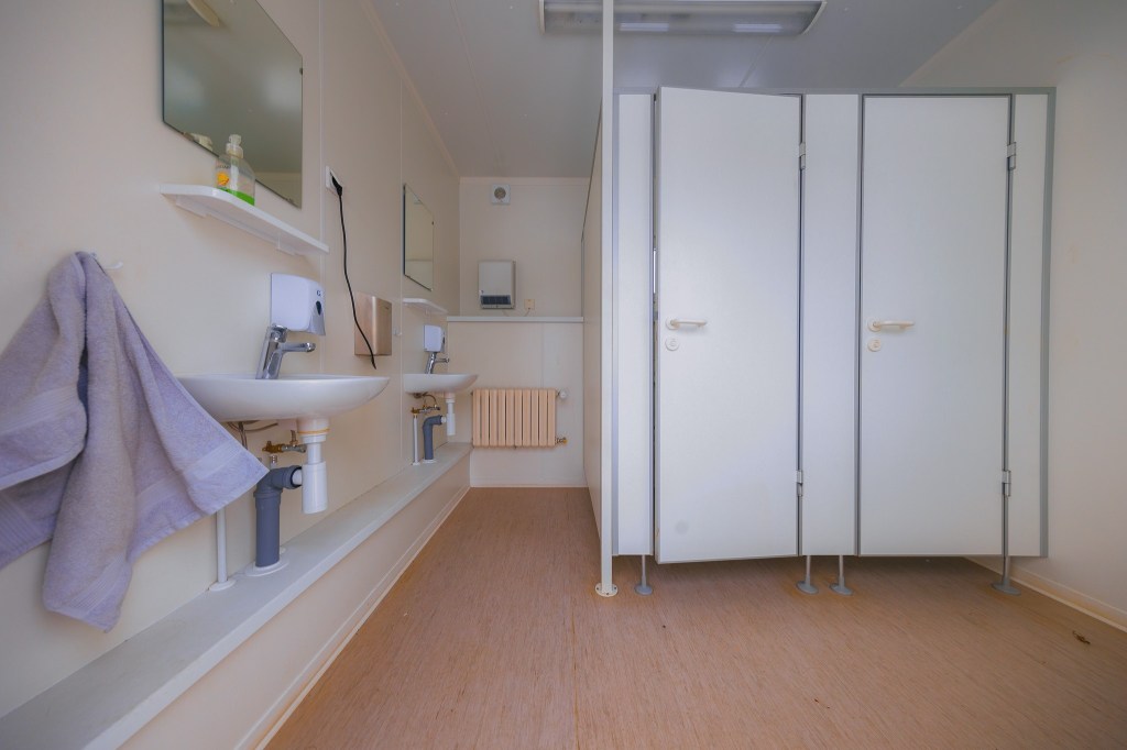 Clean bathroom with white stalls, two sinks, and mirrors on the left. Towels hang by the sinks, and soap dispensers are visible.