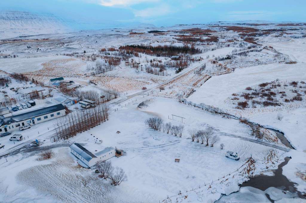Aerial view of a snowy landscape with scattered trees, winding roads, and buildings.