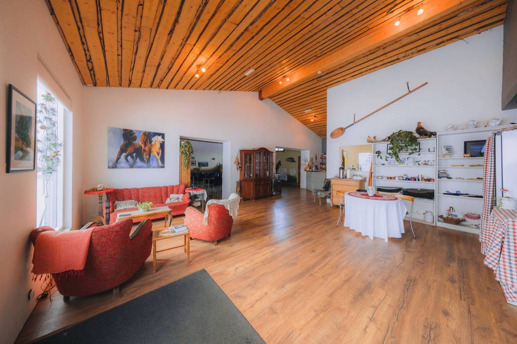 Spacious cozy room with wooden ceiling and floor, featuring red armchairs, a large cabinet, and shelves with various items. Art decorates the walls.