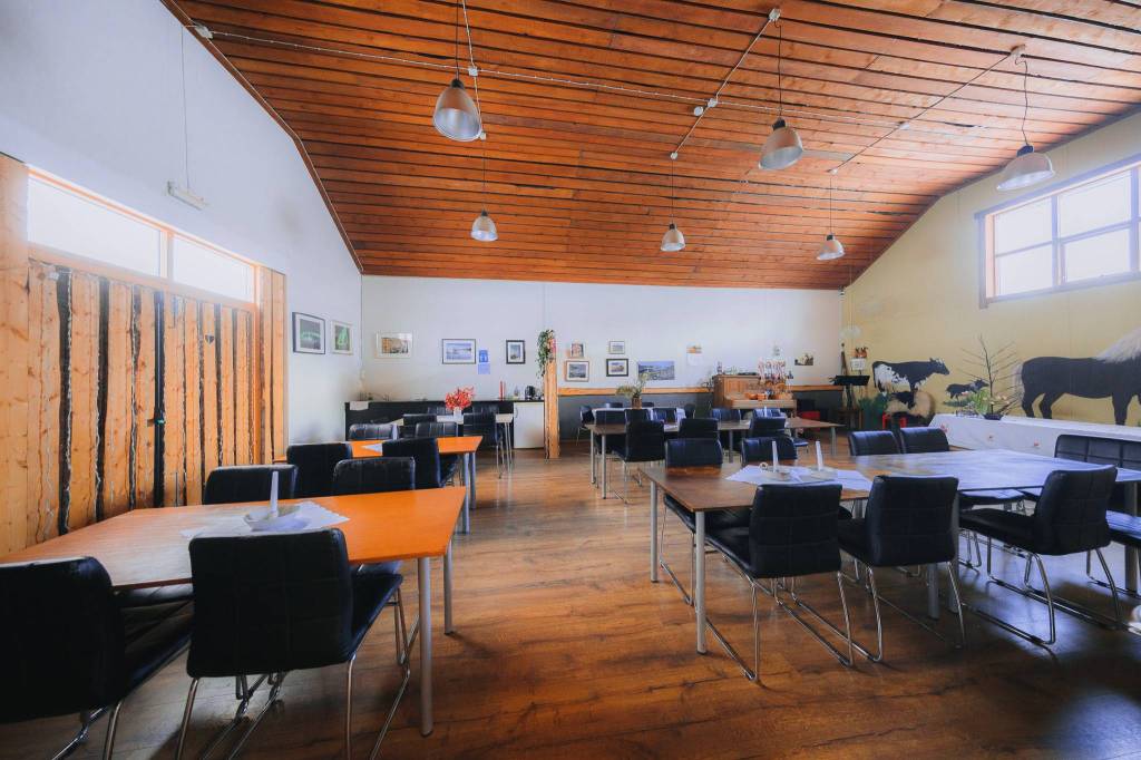 Spacious room with wooden ceiling, large windows, and pendant lights. Tables and black chairs are neatly arranged. Wall art includes horse images.