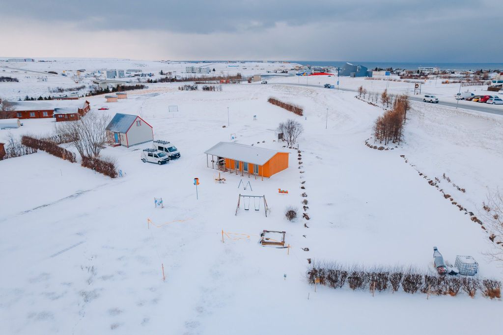 Aerial view of a snowy landscape with a small orange house surrounded by barren trees and snow-covered ground.