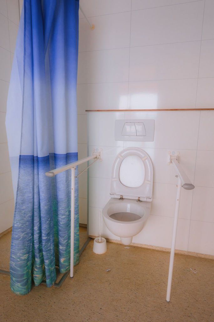 Accessible bathroom with a wall-mounted toilet, support rails, and an ocean-themed shower curtain.