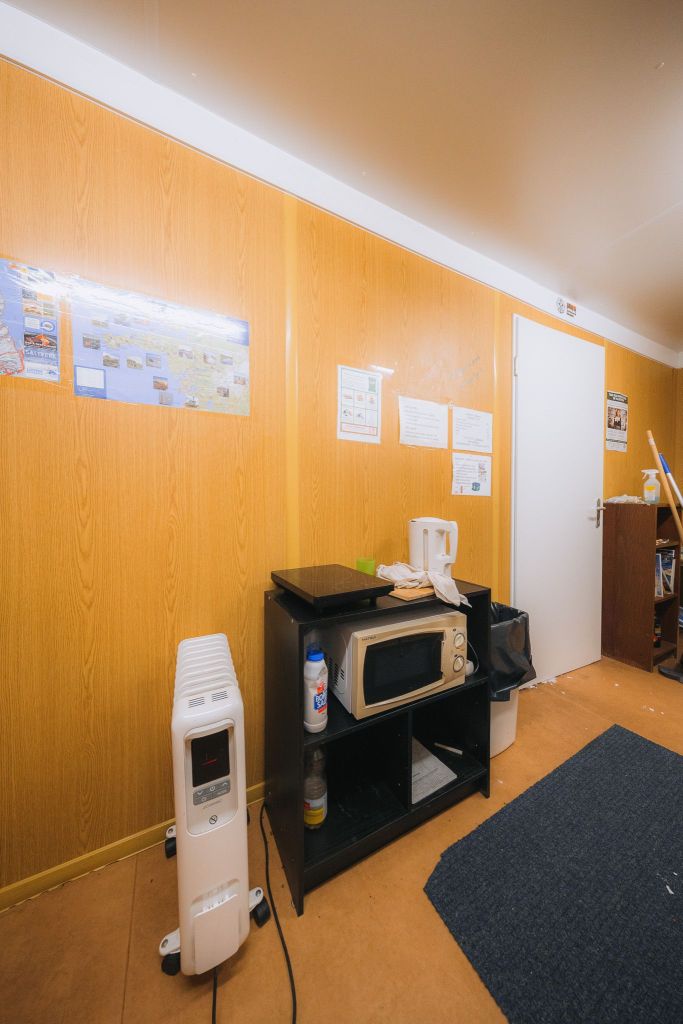 Cozy room with wooden walls featuring a heater, microwave, and kettle on a black shelf.