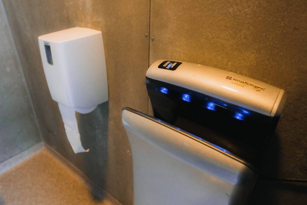 Modern public restroom with a white paper towel dispenser and a high-tech hand dryer featuring blue lights, set against a concrete wall.
