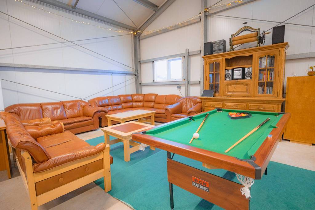Cozy recreation room with leather sofas, wooden coffee table, and a green felt pool table. A wooden cabinet with a stereo system is in the background.