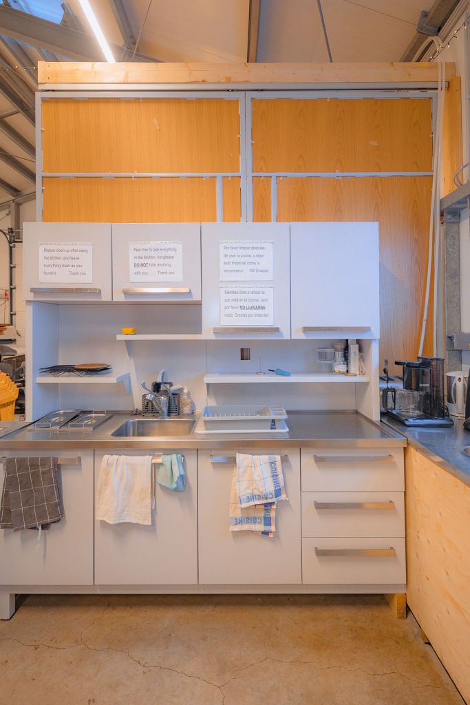 Modern kitchen with white cabinets and stainless steel countertop. Towels hang from the handle, and there are note signs on the cabinet doors.