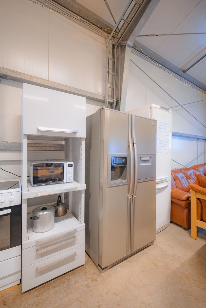 A modern kitchen corner features a stainless steel fridge, a white cabinet with a microwave, and a stove.