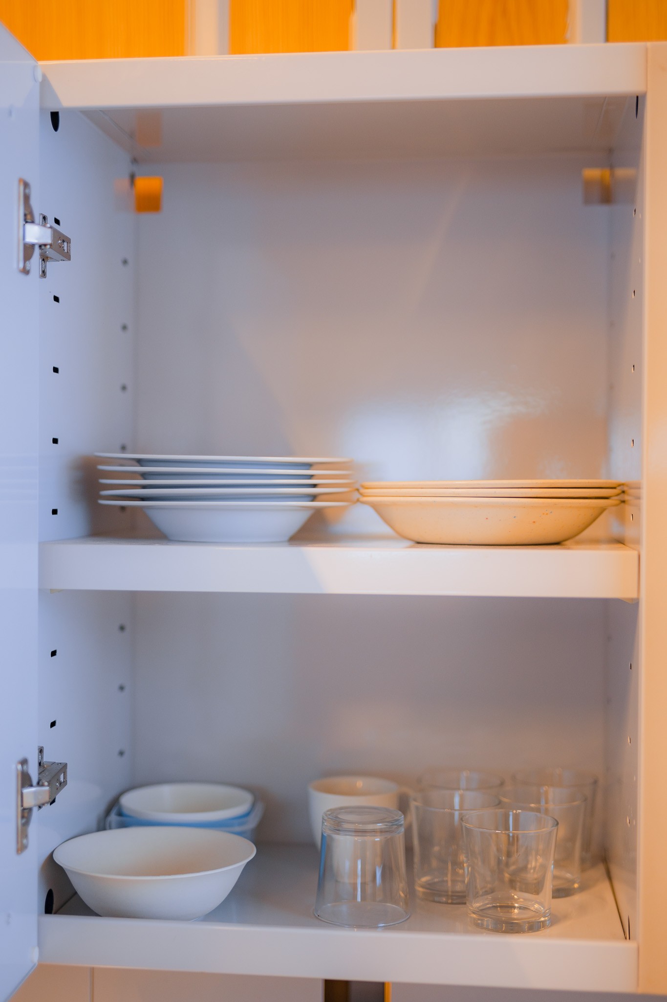 Open kitchen cabinet with neatly stacked plates on the top shelf and bowls with glasses on the bottom.