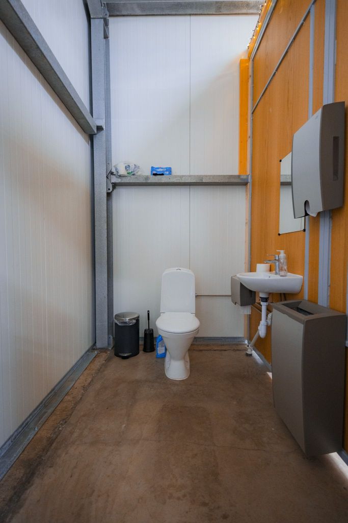 Compact bathroom with white toilet, small sink, and mirror on wooden wall.