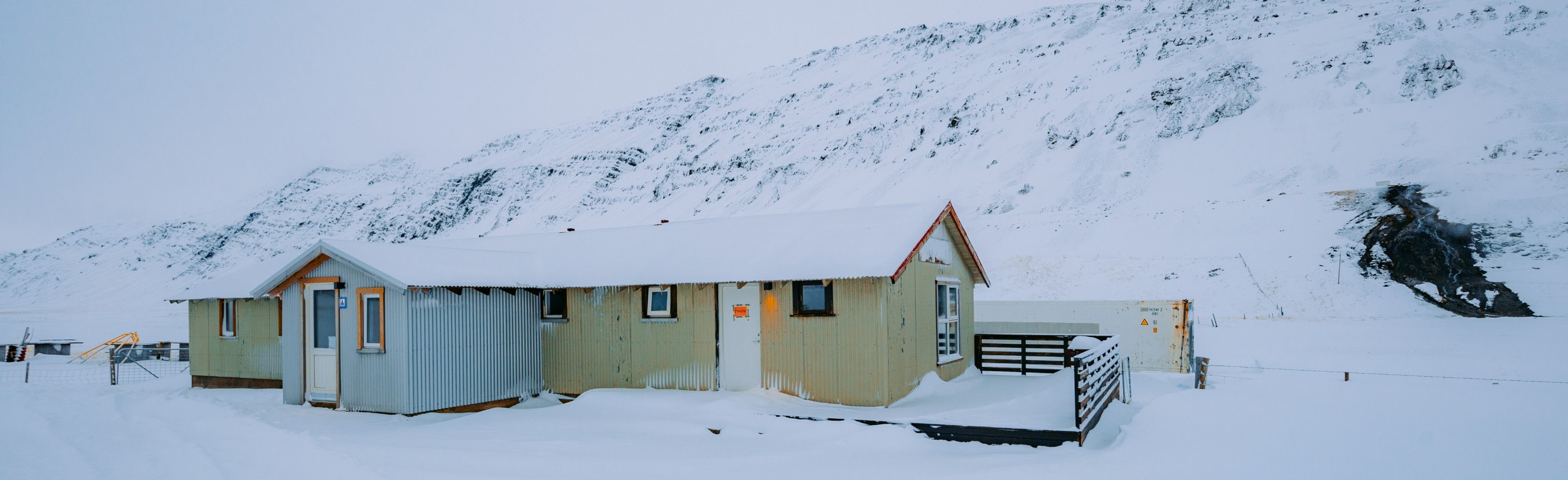 Remote cabin in a snow-covered landscape with a mountainous backdrop.