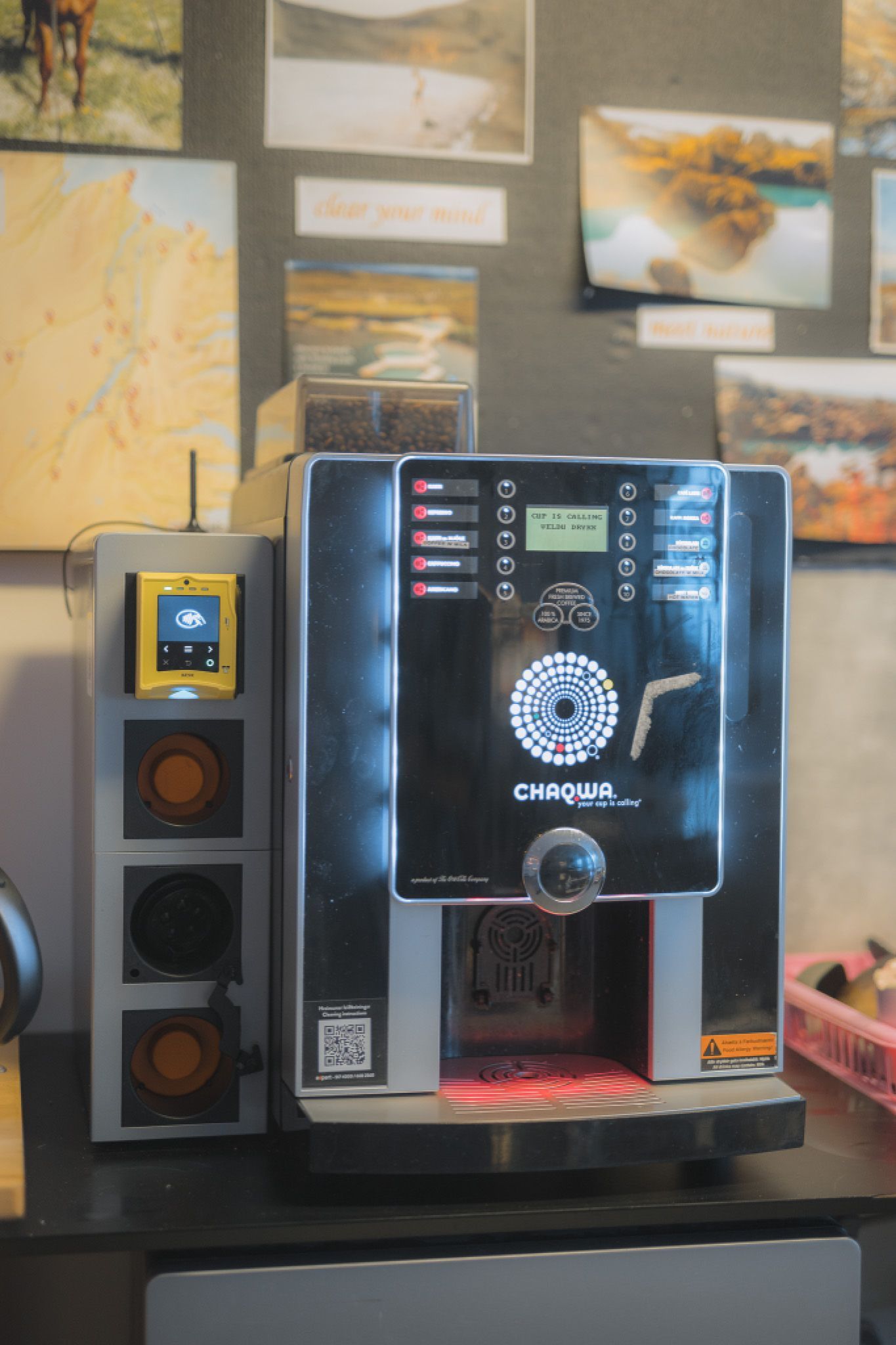 A modern coffee machine, labeled "CHAQWA," sits on a counter. It is surrounded by travel-themed photos.