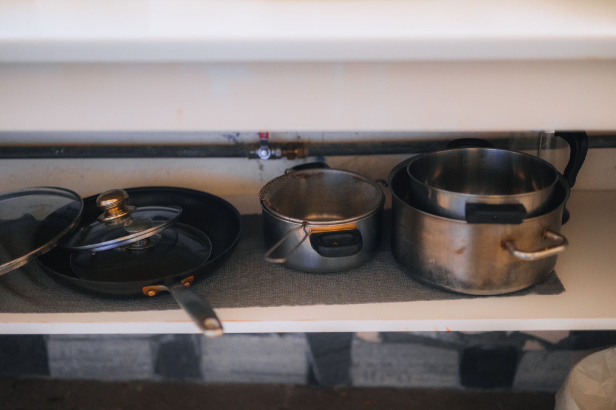 A shelf with a frying pan, saucepan, and large pot, all with black handles, neatly arranged on a gray mat.