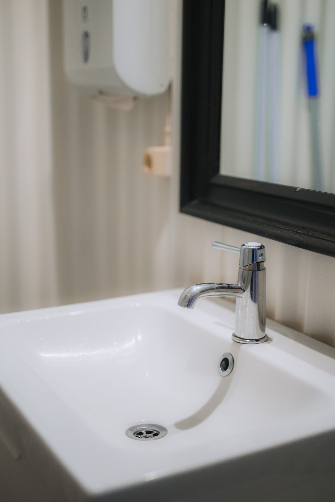 Modern bathroom sink with a sleek chrome faucet and a black-framed mirror. A soap dispenser is mounted on the wall, lending a clean, minimalist feel.