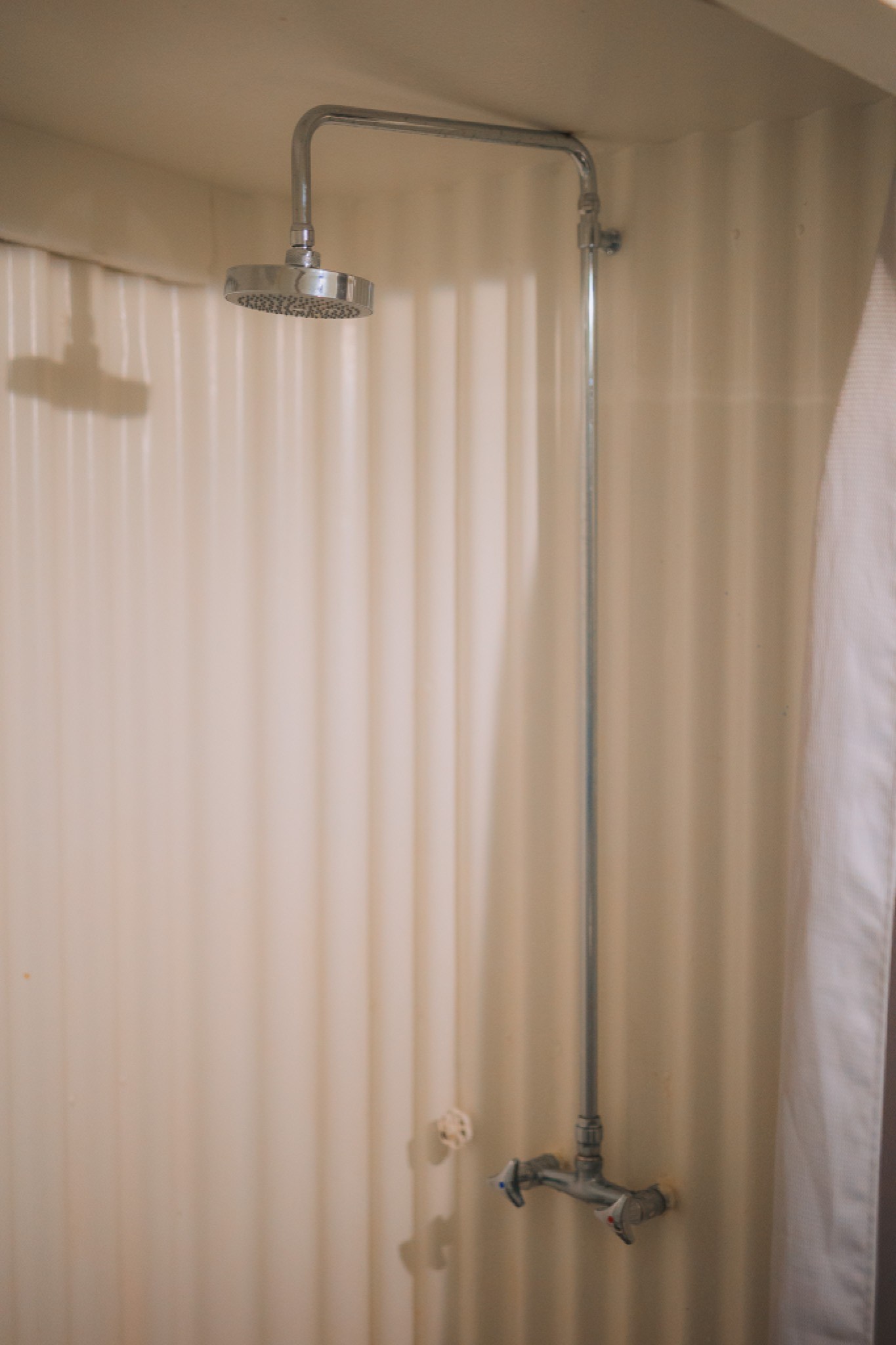 A simple, chrome showerhead with a long pipe is mounted on a beige, corrugated wall.