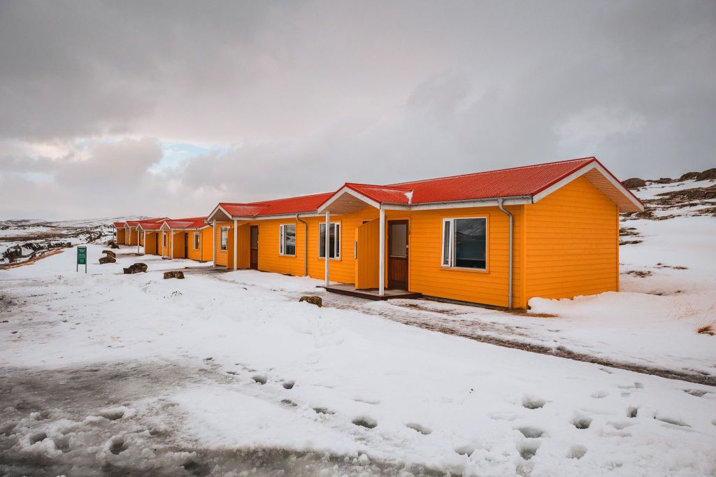 A row of bright yellow cabins with red roofs sits on a snowy landscape under a cloudy sky.