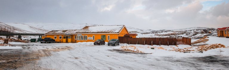 A vibrant yellow building sits amid a snowy landscape, with parked cars and a cloud-filled sky.