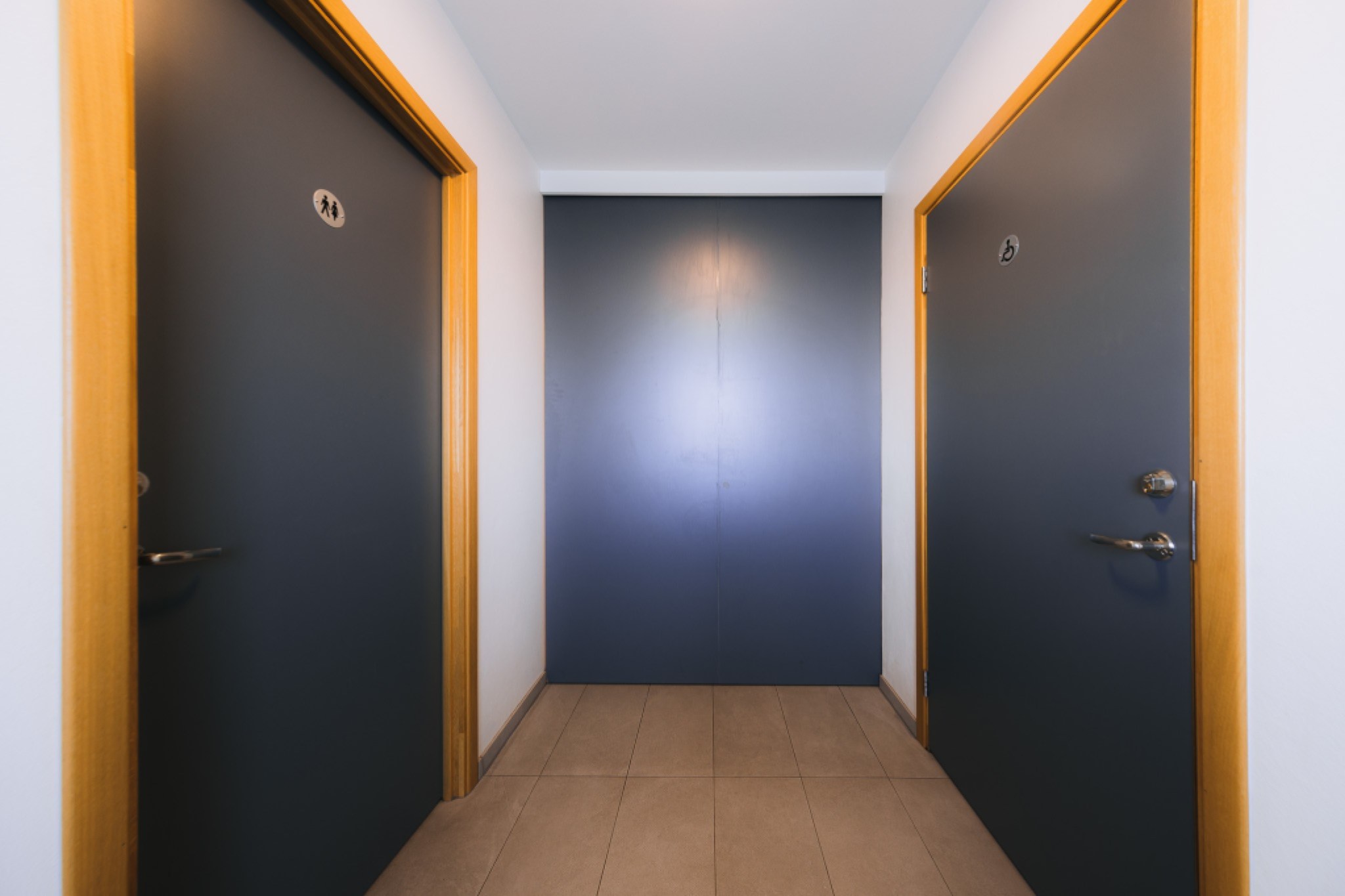 Hallway with two gray restroom doors on opposite sides, framed in light wood.