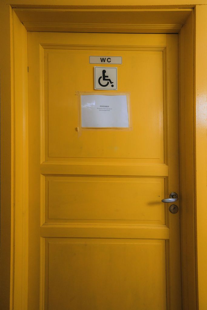 Bright yellow door with "WC" and wheelchair accessible signs, indicating a restroom. A paper notice is centered on the door.