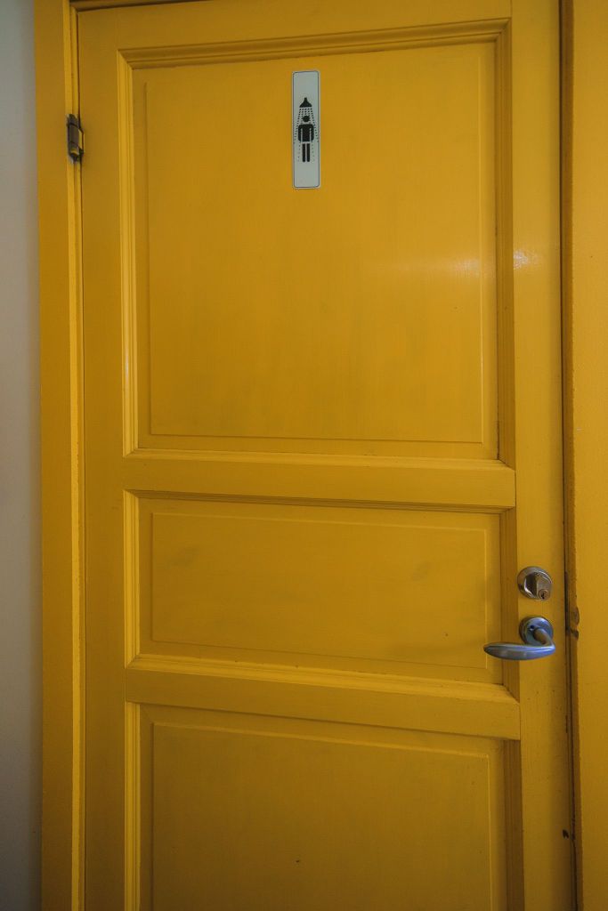 A solid yellow door with a metallic handle, featuring a black and white female restroom sign on top.