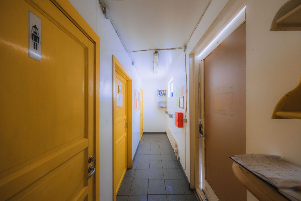 Narrow hallway with bright yellow doors on the left, a white wall on the right, and fluorescent lighting.