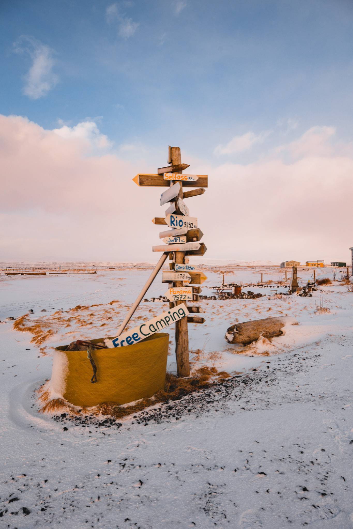 Snowy landscape with a wooden signpost displaying multiple destination arrows, including "Free Camping."