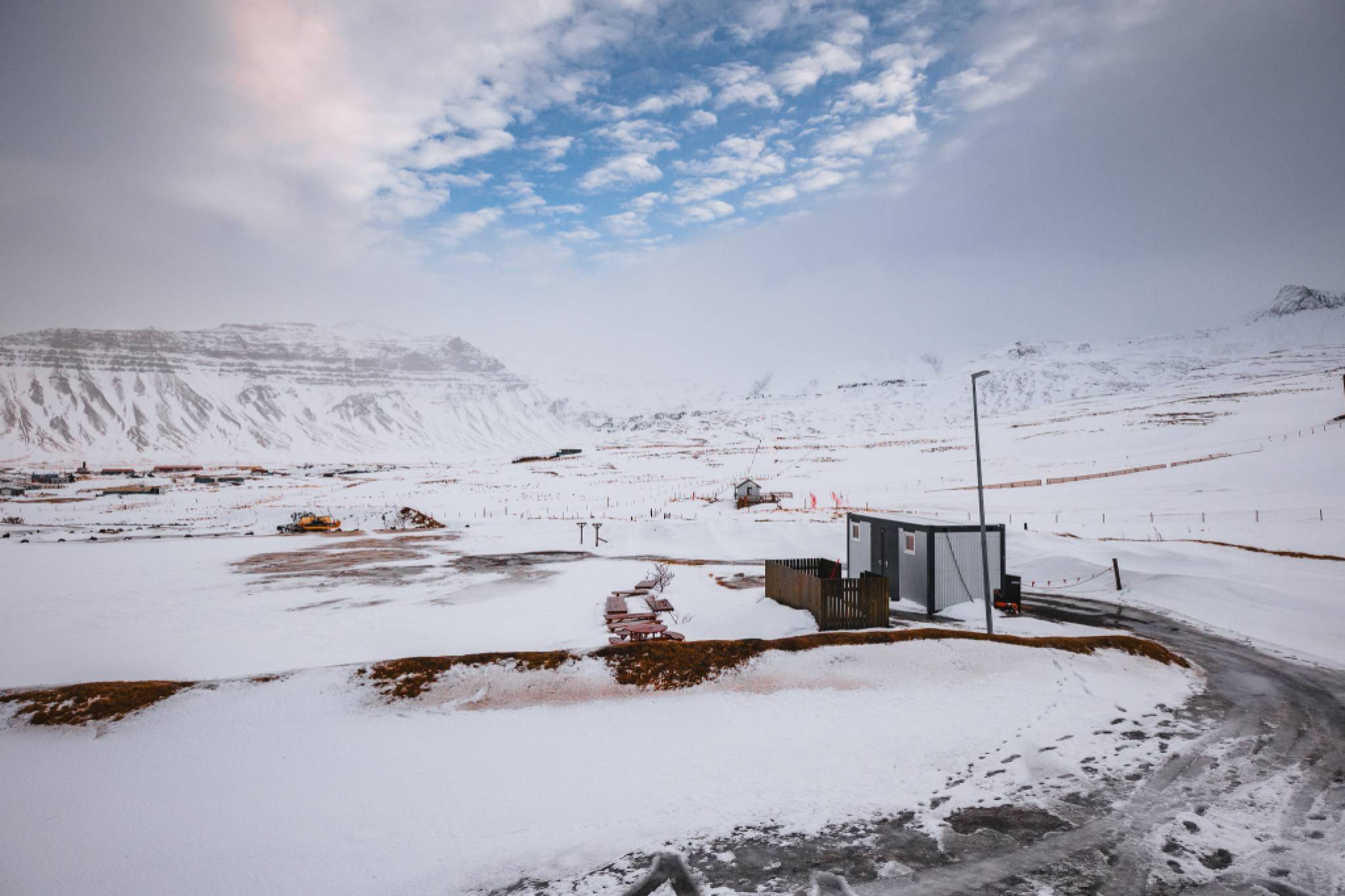 Snowy landscape with mountains in the background, a construction site with machinery, and a small building.
