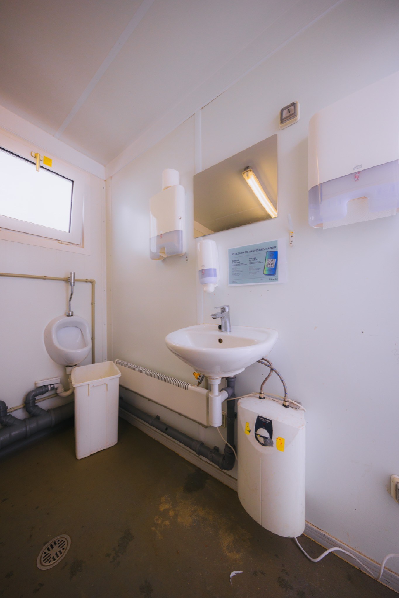 Small, clean public restroom with a sink and urinal. Dispensers and a mirror are above the sink.