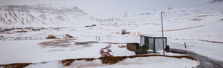 Snowy landscape with mountains in the background, a construction site with machinery, and a small building.